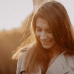 A young woman smiling softly in the warm golden sunlight during sunset outdoors.