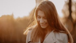 A young woman smiling softly in the warm golden sunlight during sunset outdoors.