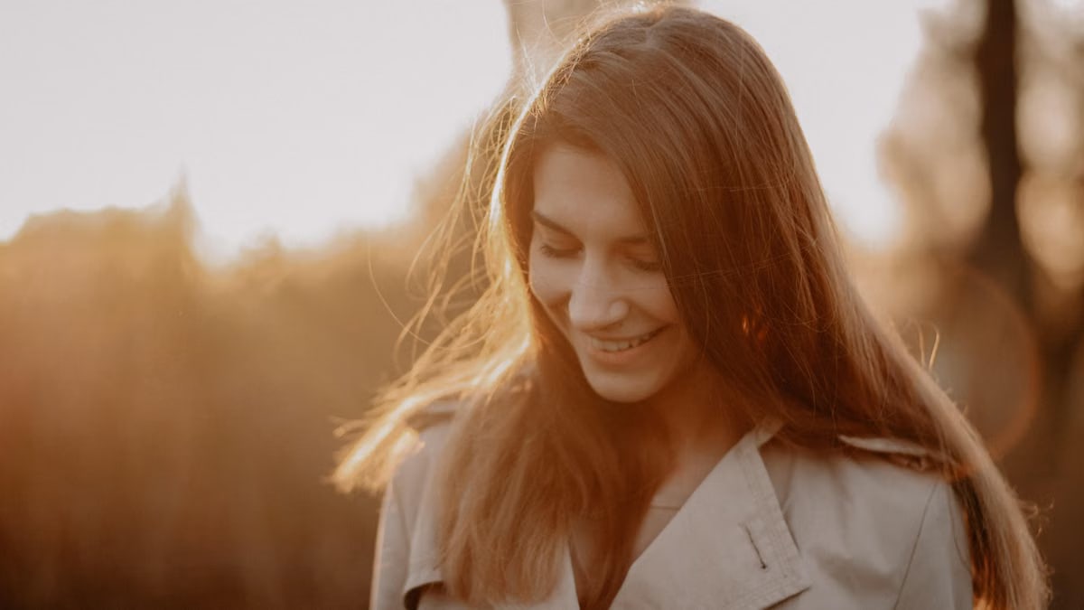 A young woman smiling softly in the warm golden sunlight during sunset outdoors.